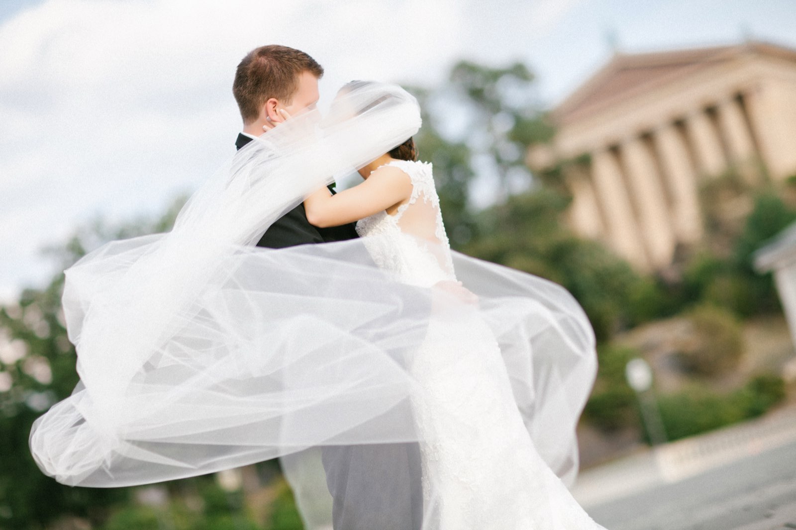 Bride and groom embracing with veil blowing in the wind at the Philadelphia Art Museum