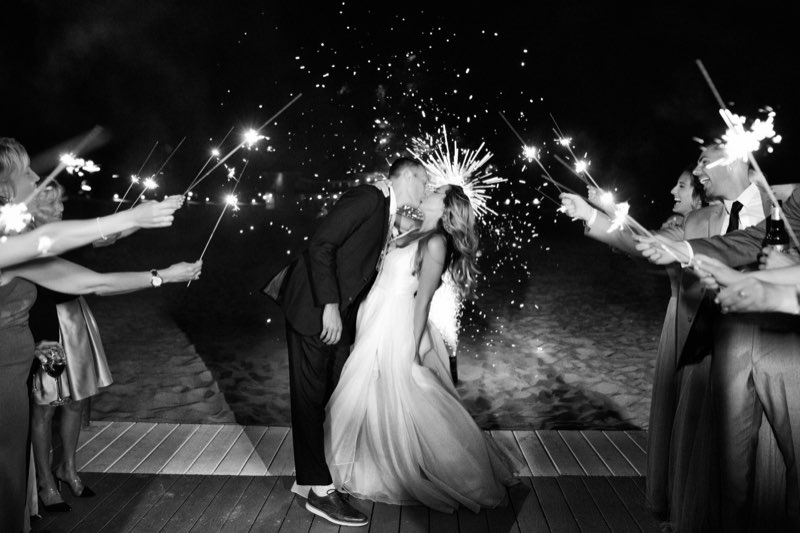 Couple sharing a sparkler exit kiss on the beach at night